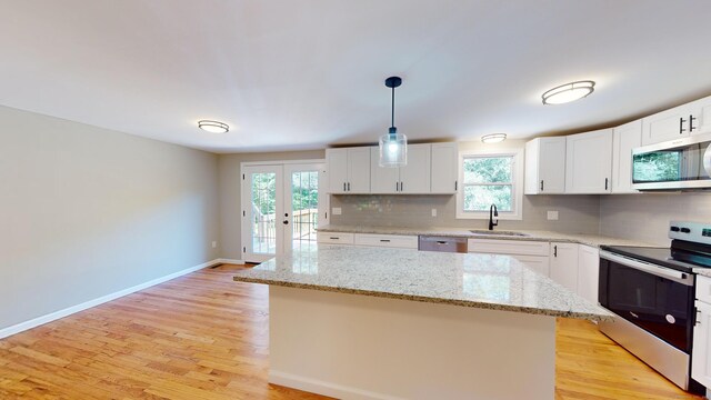 kitchen with a kitchen island, pendant lighting, appliances with stainless steel finishes, sink, and light wood-type flooring