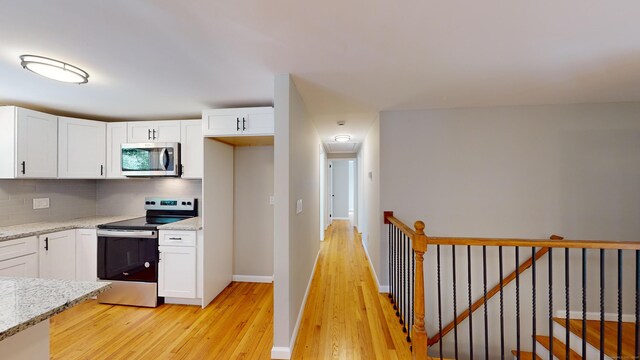 kitchen with backsplash, light stone counters, appliances with stainless steel finishes, and light hardwood / wood-style floors