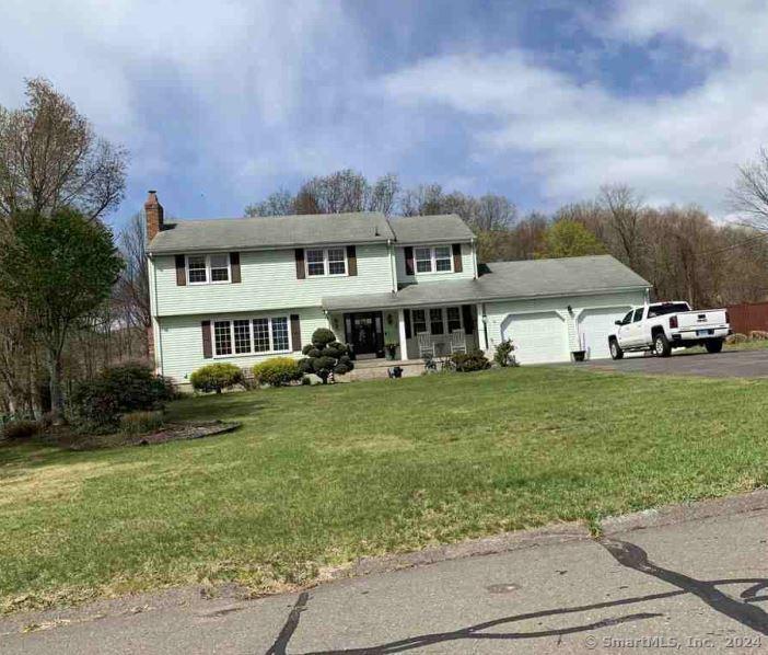 view of front of property featuring driveway, a porch, a front yard, a garage, and a chimney