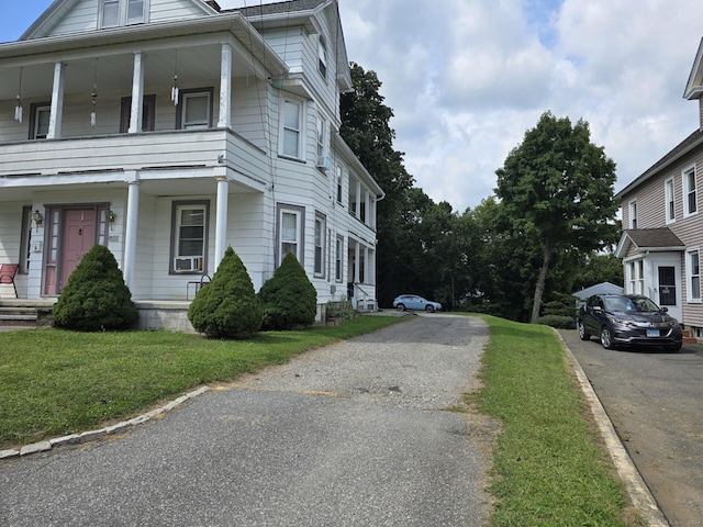 view of side of property with a porch, aphalt driveway, and a lawn