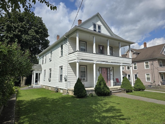 view of front facade with a porch, a balcony, a chimney, and a front lawn