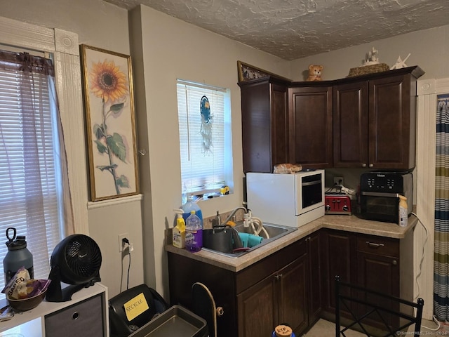 kitchen with light countertops, a healthy amount of sunlight, a sink, a textured ceiling, and dark brown cabinetry