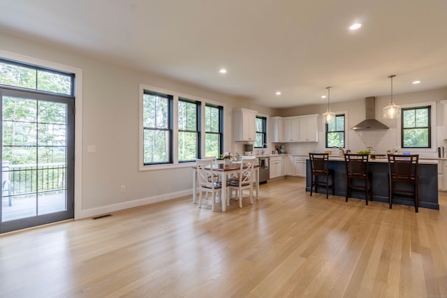 kitchen featuring wall chimney range hood, light hardwood / wood-style flooring, backsplash, stainless steel dishwasher, and white cabinetry