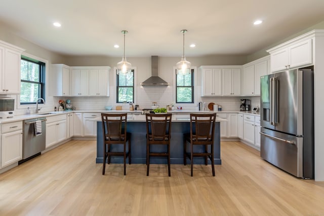 kitchen with wall chimney range hood, a healthy amount of sunlight, appliances with stainless steel finishes, and pendant lighting