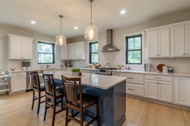 kitchen with wall chimney range hood, appliances with stainless steel finishes, plenty of natural light, and white cabinets