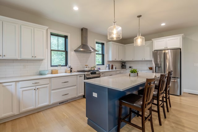 kitchen featuring a kitchen island, wall chimney exhaust hood, light hardwood / wood-style flooring, stainless steel appliances, and white cabinets