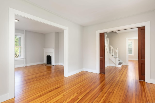 unfurnished living room featuring a fireplace with flush hearth, light wood-type flooring, baseboards, and stairs