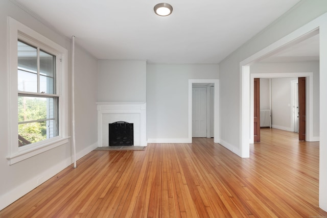 unfurnished living room featuring radiator, light wood-style flooring, a fireplace, and baseboards