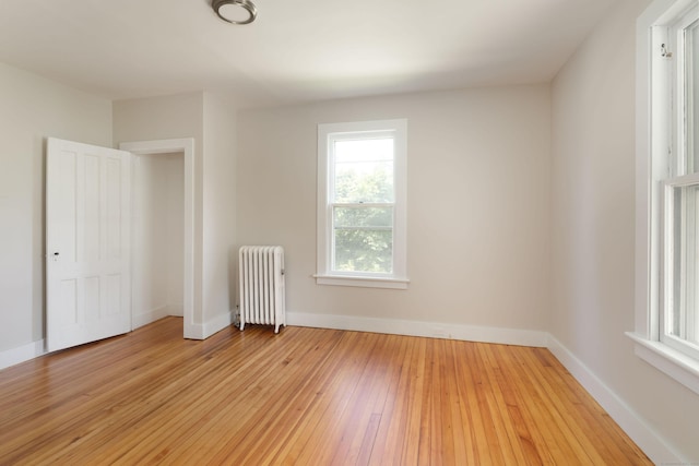 unfurnished bedroom with light wood-type flooring, baseboards, and radiator heating unit