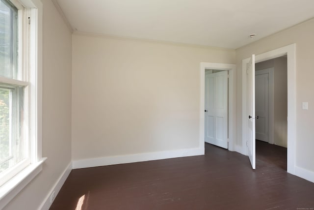 spare room with crown molding, baseboards, and dark wood-type flooring