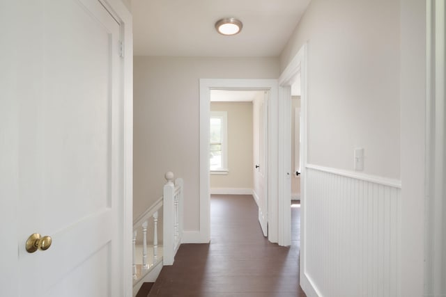 hallway with dark wood-type flooring, baseboards, and an upstairs landing