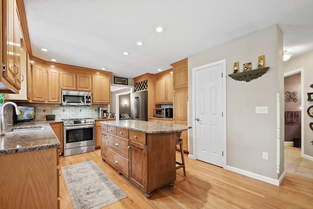 kitchen with dark stone counters, light wood-type flooring, stainless steel appliances, sink, and a center island