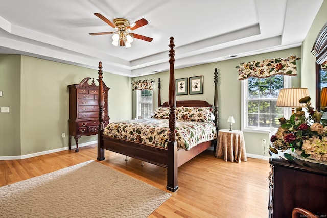 bedroom featuring ceiling fan, a raised ceiling, and light hardwood / wood-style flooring