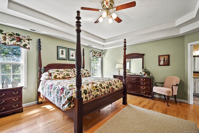 bedroom featuring ensuite bath, a tray ceiling, and light hardwood / wood-style floors