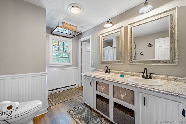 bathroom with a textured ceiling, wood-type flooring, toilet, vanity, and baseboard heating