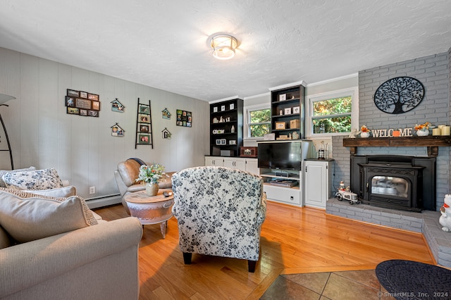 living room featuring wood-type flooring, a textured ceiling, baseboard heating, and a brick fireplace