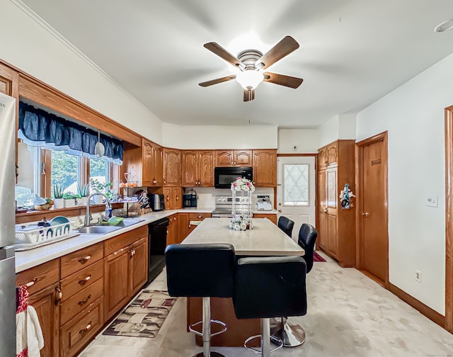 kitchen featuring a kitchen breakfast bar, black appliances, a center island, sink, and ceiling fan