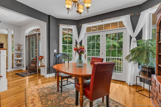 dining area with a notable chandelier, light hardwood / wood-style flooring, decorative columns, and a healthy amount of sunlight