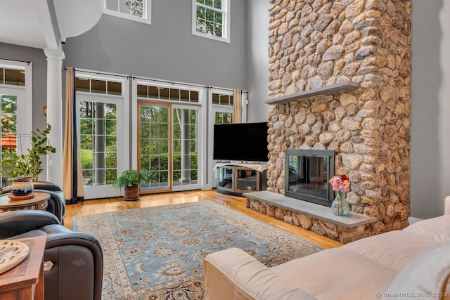 living room featuring a stone fireplace, light hardwood / wood-style flooring, and decorative columns