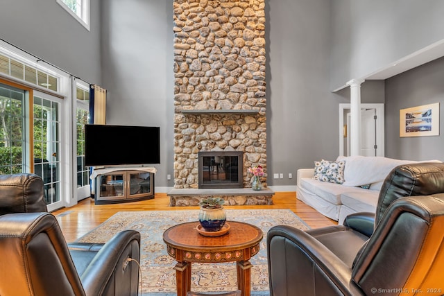 living room featuring ornate columns, light wood-type flooring, a towering ceiling, and a stone fireplace