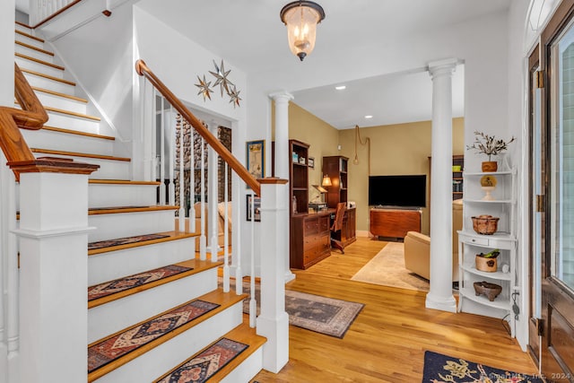 stairs with wood-type flooring, decorative columns, and a wealth of natural light