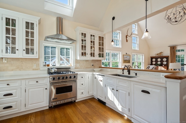 kitchen with white cabinetry, designer range, pendant lighting, sink, and wall chimney range hood