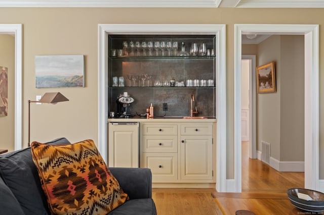 bar with sink, light hardwood / wood-style flooring, cream cabinetry, and ornamental molding