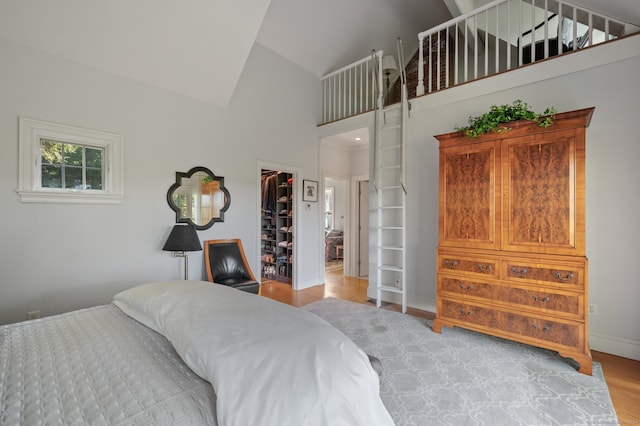 bedroom featuring light wood-type flooring, high vaulted ceiling, a walk in closet, and a closet