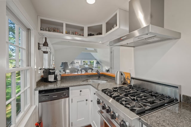 kitchen with white cabinets, sink, wall chimney range hood, stainless steel appliances, and dark stone counters