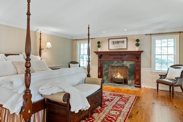 bedroom with multiple windows, a fireplace, crown molding, and light hardwood / wood-style flooring