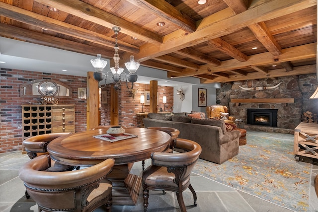 dining space with an inviting chandelier, wood ceiling, beamed ceiling, brick wall, and a stone fireplace