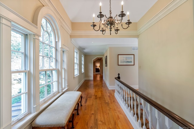 hall with crown molding, a healthy amount of sunlight, light hardwood / wood-style flooring, and a chandelier