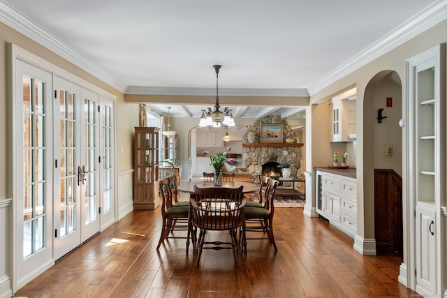 dining area featuring dark hardwood / wood-style floors, a stone fireplace, beam ceiling, and french doors