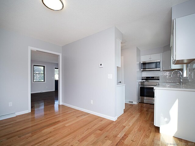 kitchen featuring light hardwood / wood-style flooring, tasteful backsplash, stainless steel appliances, sink, and white cabinetry