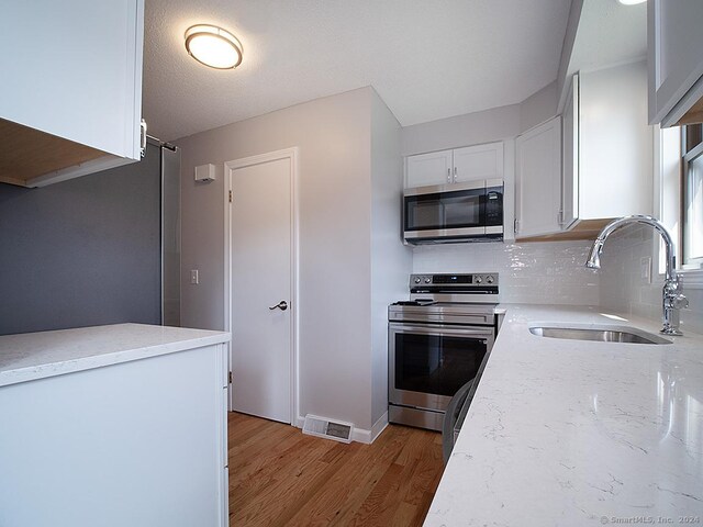 kitchen with backsplash, light hardwood / wood-style floors, stainless steel appliances, sink, and white cabinets