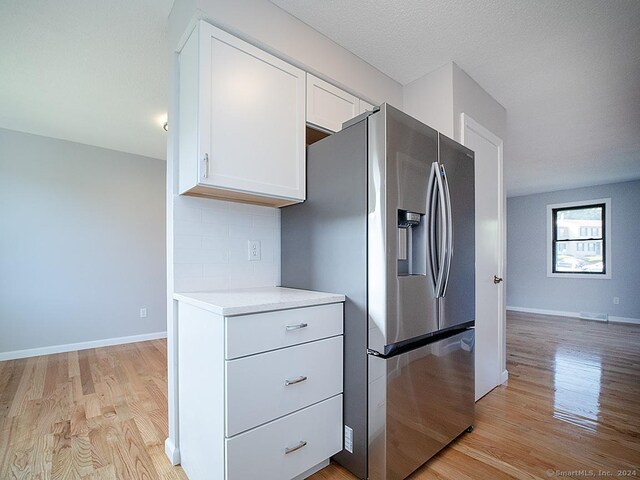 kitchen with stainless steel fridge with ice dispenser, light wood-type flooring, a textured ceiling, and white cabinets