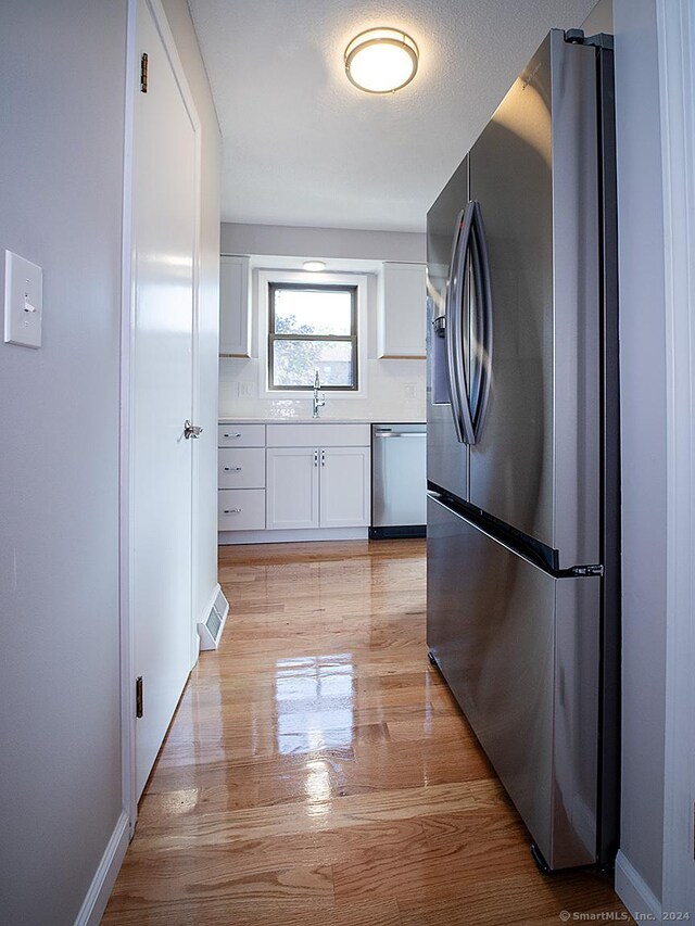 kitchen featuring light wood-type flooring, white cabinetry, stainless steel appliances, sink, and decorative backsplash