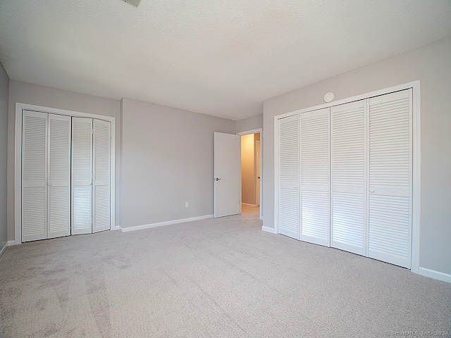 unfurnished bedroom featuring a textured ceiling, light colored carpet, and two closets