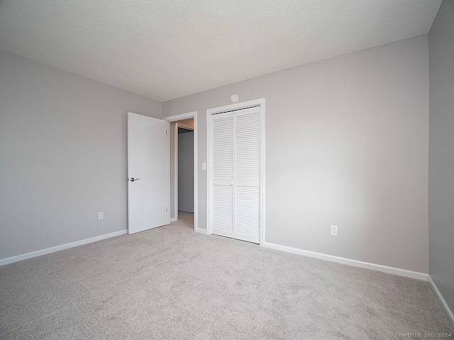 unfurnished bedroom featuring light carpet, a textured ceiling, and a closet