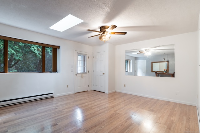 entrance foyer featuring a textured ceiling, baseboard heating, light hardwood / wood-style floors, a skylight, and ceiling fan