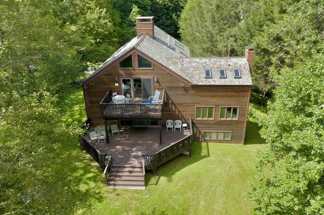 rear view of house with a wooded view, a yard, a chimney, and a wooden deck