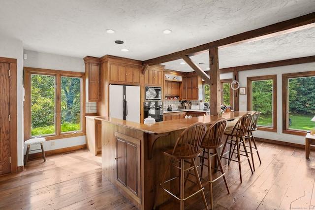 kitchen with built in microwave, white refrigerator, black oven, decorative backsplash, and light wood-type flooring