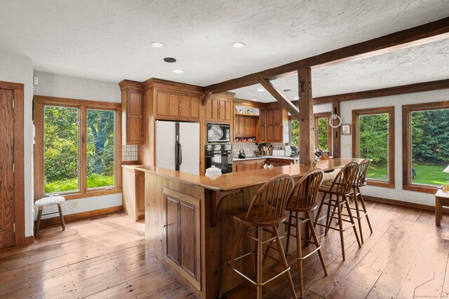 kitchen with brown cabinets, tasteful backsplash, freestanding refrigerator, built in microwave, and black oven