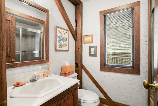 bathroom with a textured wall, a shower stall, toilet, and vanity