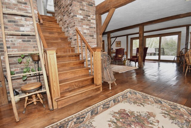 staircase with beam ceiling, wood-type flooring, and a textured ceiling