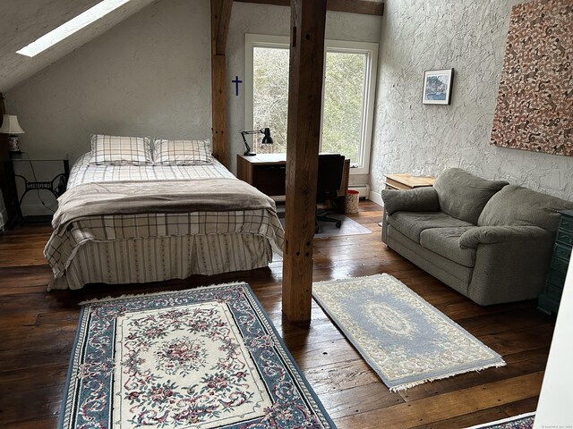 bedroom with hardwood / wood-style flooring, vaulted ceiling with skylight, and a textured wall