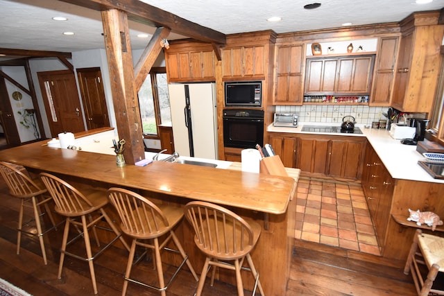 kitchen featuring black appliances, beam ceiling, a kitchen bar, and butcher block countertops