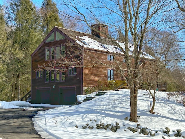 view of snowy exterior featuring a garage and a chimney