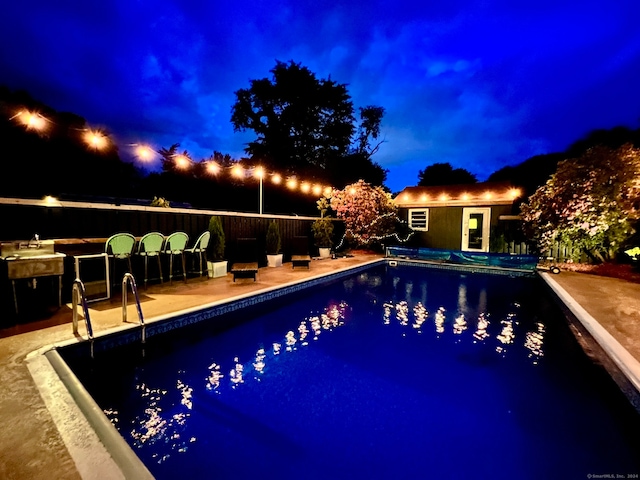 pool at twilight with area for grilling and a patio area