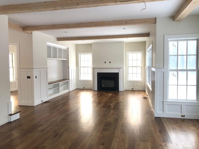 unfurnished living room with beamed ceiling, plenty of natural light, dark wood-type flooring, and built in shelves